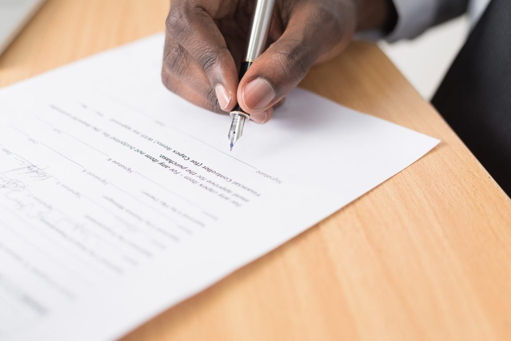A person holding pen to sign a HR consulting and outsourcing document on brown table.