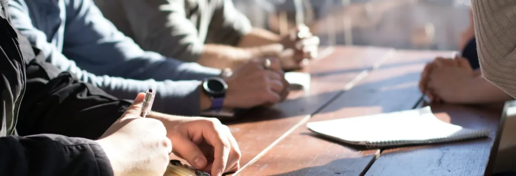 A diverse group of professionals sitting at a table with a notebook during an HR Services meeting.
